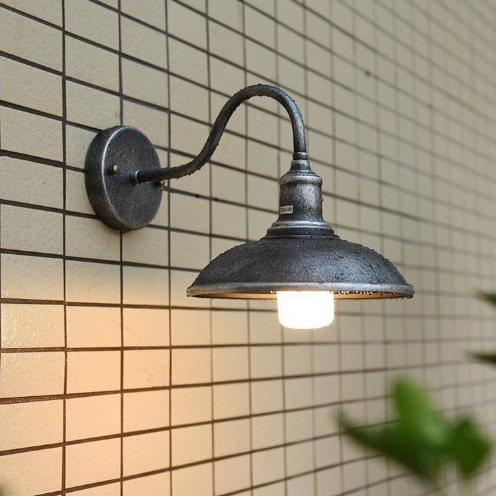 Rund, lokkformet vegglampe med buet jernskjerm og enkeltflammedesign for terrassen